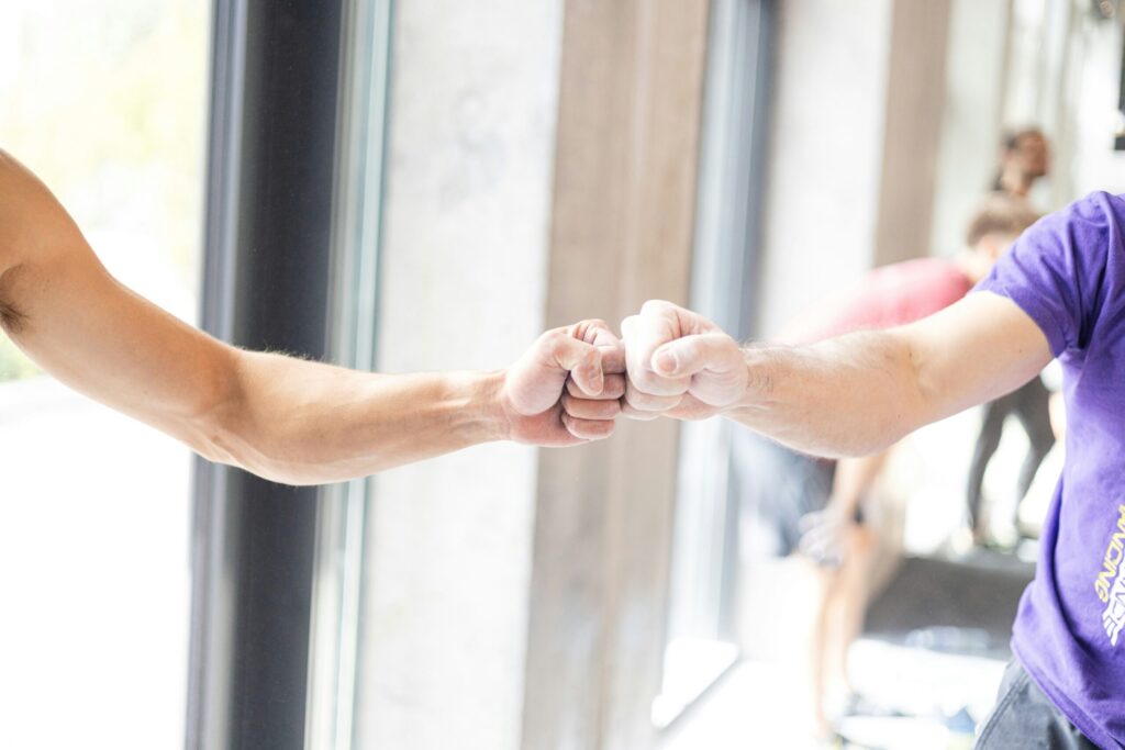 Two gym-goers fist bumping in a welcoming, low-key gym setting, representing the kind of everyday ease an inclusive gym should feel like