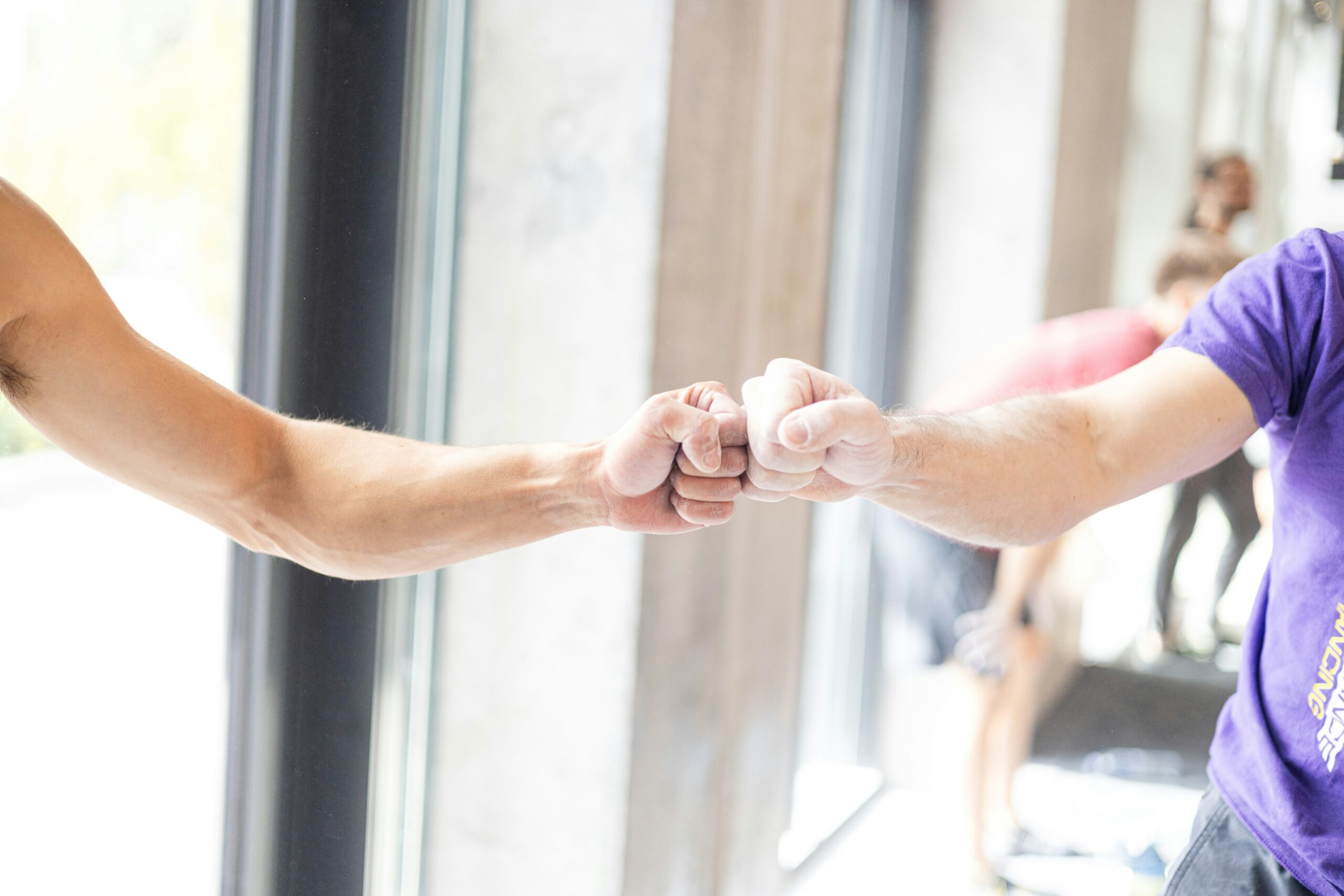 Two gym-goers fist bumping in a welcoming, low-key gym setting, representing the kind of everyday ease an inclusive gym should feel like