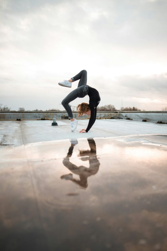 A person in a full backbend, joints extended, reflected in a puddle of water below