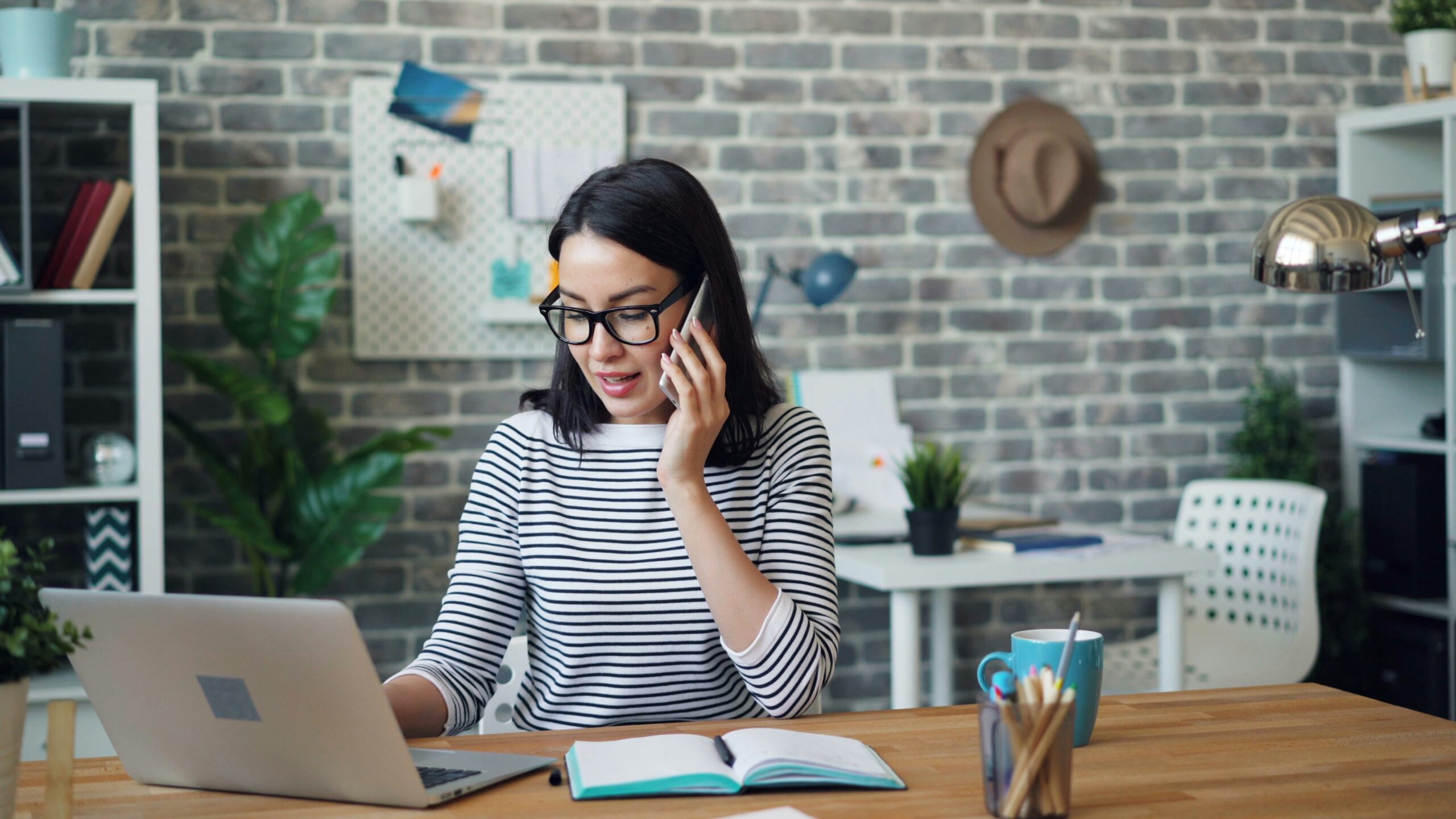 A person taking notes while on the phone and looking at a laptop, representing the work of documenting a healthcare visit and following up afterward